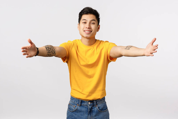 Come here let me hug you. Tender and touched charming lovely asian guy with tattoos, welcoming someone, extend arms sideways to hug deares friend, smiling friendly, standing white background cuddling - Foto, immagini