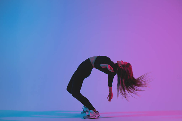 Sporty woman dancing in studio against colorful phantom blue color background. Young athletic girl dancer posing  - 写真・画像