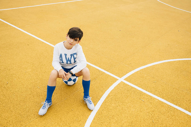Portrait of soccer player boy sitting on the ball - Фото, изображение