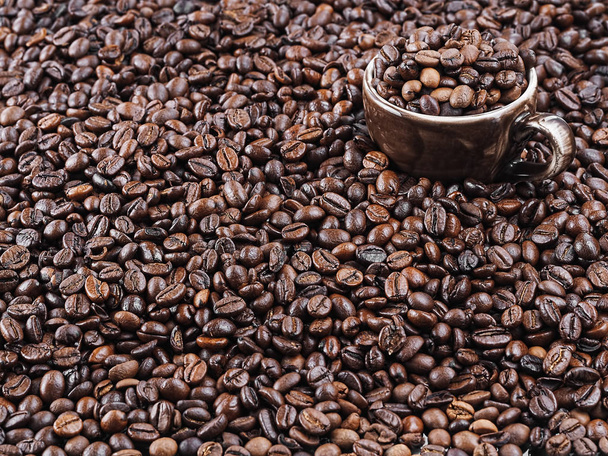 Granos de café tostados, fondo. Orientación horizontal. Café oscuro aromático fresco. Una taza marrón para café espresso se encuentra en granos de café. Primer plano. Enfoque selectivo en una taza con granos de café
. - Foto, Imagen