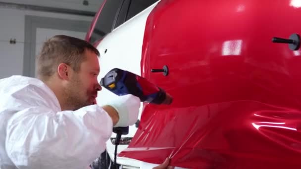 εργαζόμενος άνθρωπος θερμαίνει ταινία βινυλίου από τον ανεμιστήρα και τον καθορισμό στην πόρτα του αυτοκινήτου - Πλάνα, βίντεο