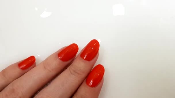 Clavos rojos, manicura clásica, mano femenina sobre una superficie blanca con agua, día de spa
 - Metraje, vídeo
