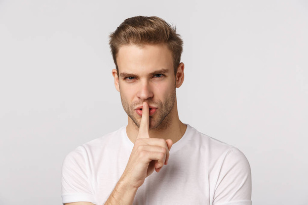 Close-up studio portrait blond handsome, sassy bearded guy squinting displeased, look strict and bossy, shushing, press index finger to lip telling be quiet, stay silent, keep secret, hushing - Фото, изображение