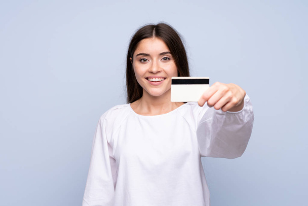 Young woman over isolated blue background holding a credit card - Foto, immagini