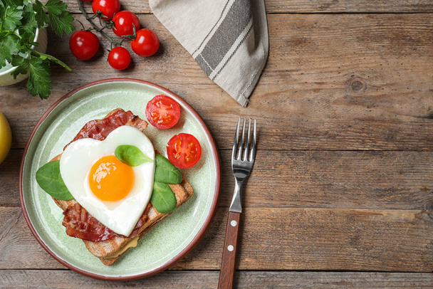 Tasty sandwich with heart shaped fried egg and bacon on wooden table, flat lay. Space for text - Foto, Bild