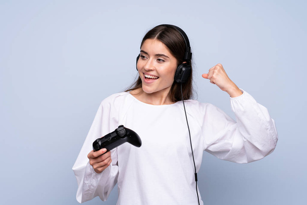 junge Frau über isoliertem blauem Hintergrund spielt bei Videospielen - Foto, Bild