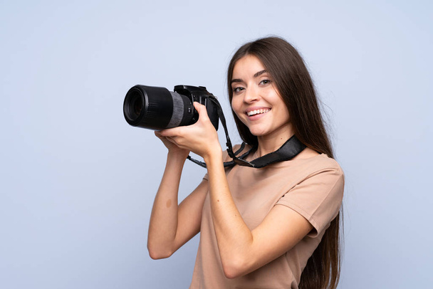 Jonge vrouw over geïsoleerde blauwe achtergrond met een professionele camera - Foto, afbeelding