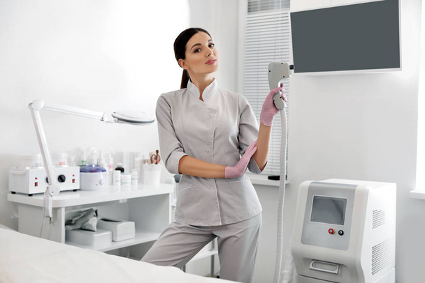 Young woman holding professional laser epilator in beauty salon - Foto, Imagem