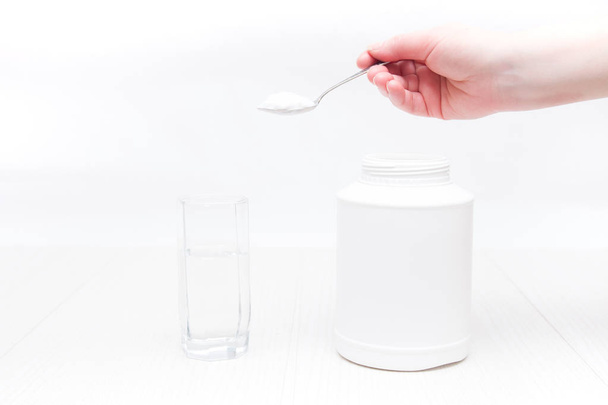 jar and glass of water on a white background, a hand holds a spoon and pours powder into a glass of water, absorbent treatment concept - Foto, Bild