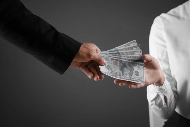 Man giving bribe money to woman on dark background, closeup - Φωτογραφία, εικόνα