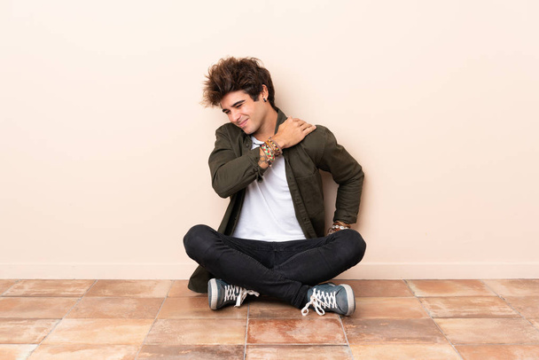 Jeune homme caucasien assis sur le sol souffrant de douleur à l'épaule pour avoir fait un effort
 - Photo, image