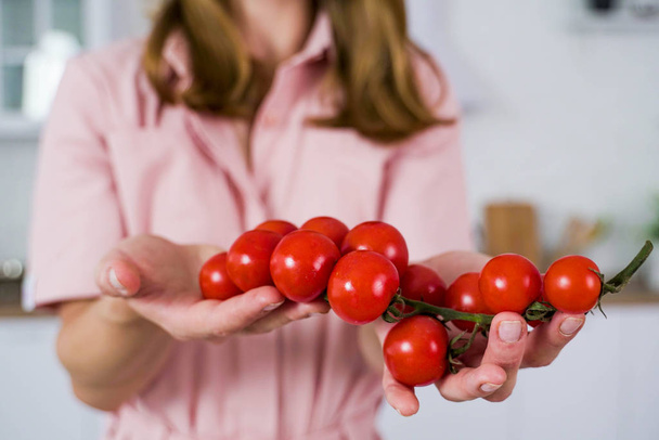 A large branch of red cherry tomato in the hands of a girl. - Zdjęcie, obraz