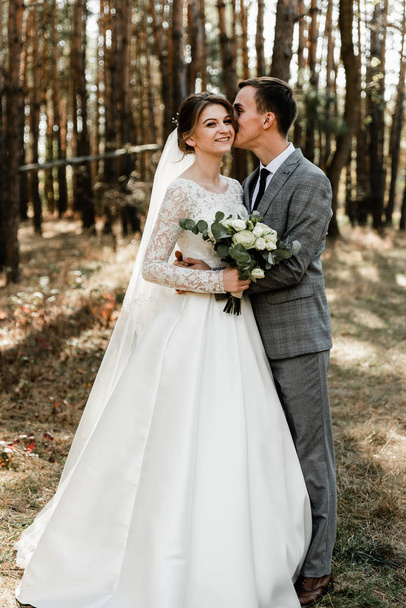 Attractive couple celebrating their wedding in forest. Portrait of young happy groom and bride in wedding clothes standing together, holding hands and looking at each other - Fotoğraf, Görsel