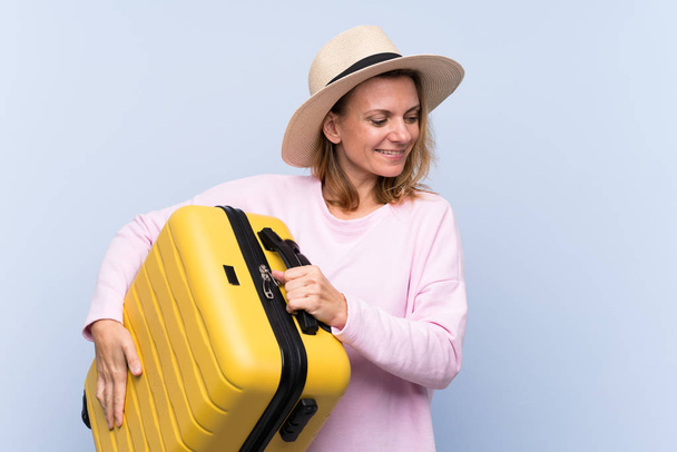Blondýny žena přes izolované pozadí v dovolené s cestovní kufr a klobouk - Fotografie, Obrázek