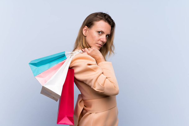Mulher loira sobre isolado fundo azul segurando sacos de compras
 - Foto, Imagem