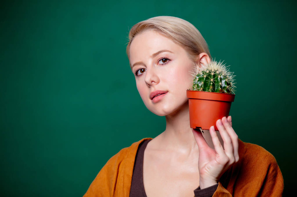 woman holds cactus in her hand near a face on green background - 写真・画像