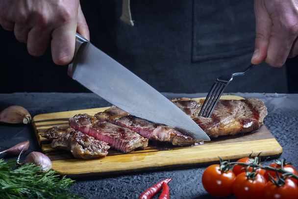 A chef cuts a freshly prepared steak into pieces. The meat is medium rare. Delicious restaurant meal - Фото, изображение