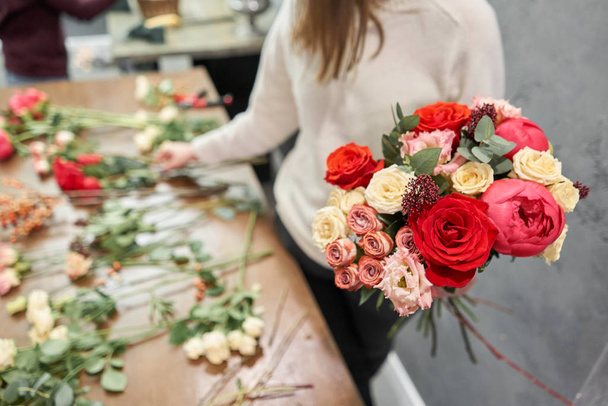 Βήμα-βήμα ανθοπώλης γυναίκα δημιουργεί κόκκινο όμορφο μπουκέτο από μικτή λουλούδια. Ωραία φρέσκια παρέα. Εκπαίδευση, master class και floristry μαθήματα. Παράδοση λουλουδιών. Ευρωπαϊκή ιδέα ανθοπωλείου. - Φωτογραφία, εικόνα