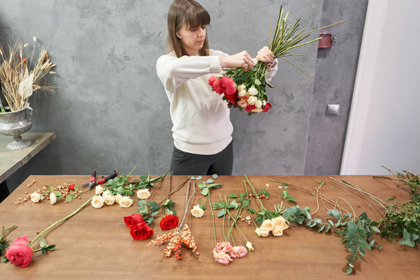 European floral shop concept. Florist woman creates red beautiful bouquet of mixed flowers. Handsome fresh bunch. Education, master class and floristry courses. Flowers delivery. - Foto, afbeelding