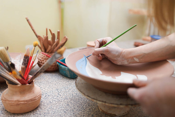  Potter mujer pinta un plato de cerámica. Chica dibuja con un cepillo en loza. Proceso de creación de productos de arcilla
. - Foto, Imagen