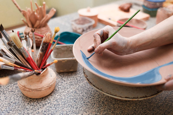 Potter mujer pinta un plato de cerámica. Chica dibuja con un cepillo en loza. Proceso de creación de productos de arcilla
 - Foto, Imagen