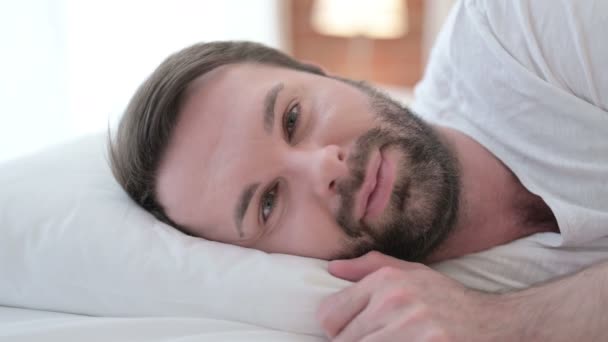 close-up van vrolijke baard jongeman glimlachen bij camera in bed - Video