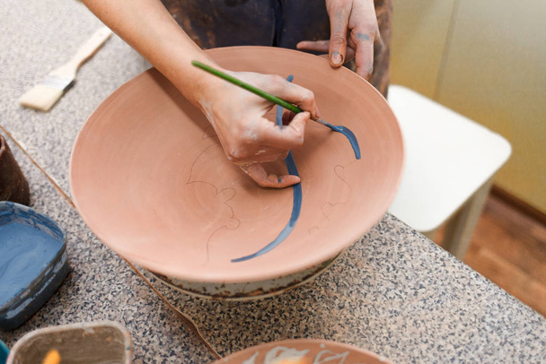 Potter donna dipinge un piatto di ceramica primo piano. Ragazza disegna con un pennello su terracotta. Processo di creazione di prodotti argillosi
. - Foto, immagini