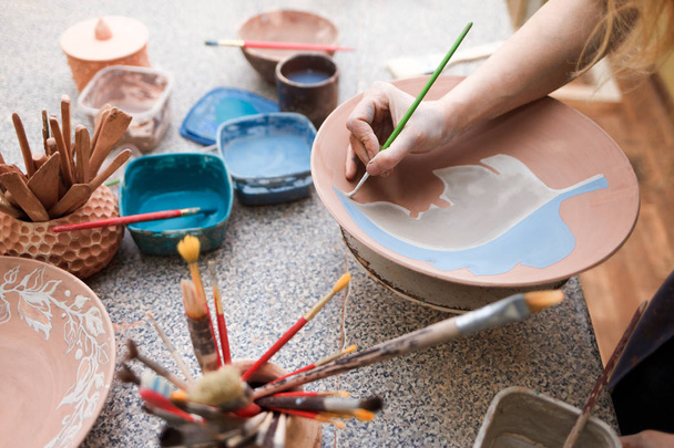Potter namalowała ceramiczną płytę. Dziewczyna rysuje pędzlem na ceramice. Proces wytwarzania wyrobów z gliny - Zdjęcie, obraz