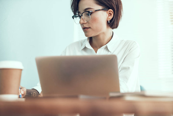 Jonge vrouw zit met laptop op kantoor - Foto, afbeelding