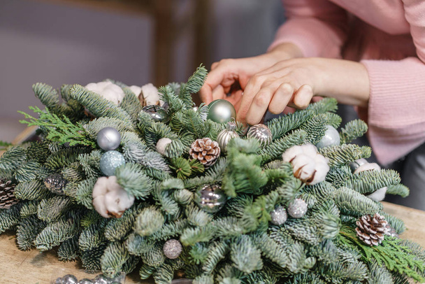 Eine Frau schmückt ein weihnachtliches Gesteck. Hände aus nächster Nähe. Meisterkurs in der Herstellung dekorativer Ornamente. Weihnachtsdekoration mit ihren eigenen Händen. das Neujahrsfest. Blumenladen - Foto, Bild