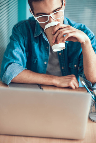 Young man is drinking coffee at workplace - Фото, зображення