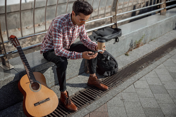 Guitarist holding mobile phone and enjoying coffee - Foto, Imagen