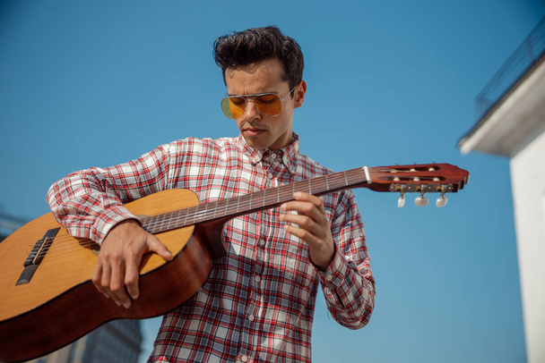 Stylish young guy holding a guitar outdoors - Фото, зображення