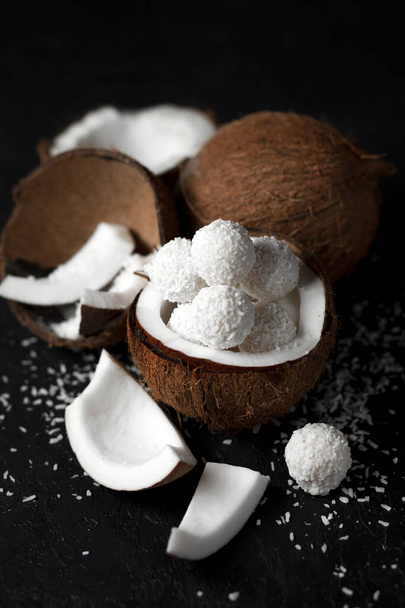 keitetyt kookosmaitokarkit mustalla tummalla pohjalla, jälkiruoan ainesosat kookospähkinöillä, makea tuote kookoshiutaleilla
 - Valokuva, kuva