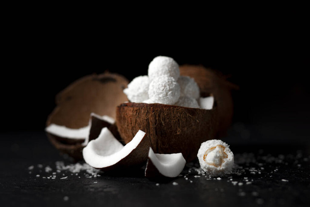 cooked coconut milk candies on a black dark background, ingredients for a dessert with coconuts, a sweet product with coconut flakes - Foto, Imagen