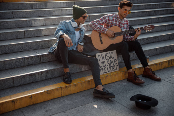 Stylish musicians is playing guitar on the street - Photo, Image