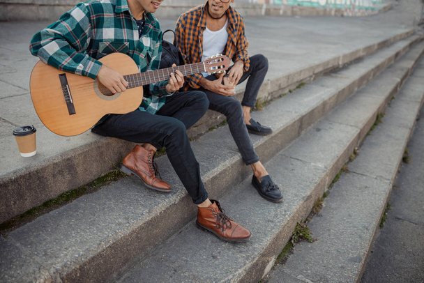 Smiling two male friends sitting on steps with guitar - Zdjęcie, obraz