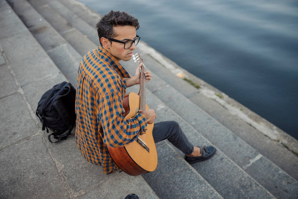 Stylish guy in glasses playing guitar outdoors - Zdjęcie, obraz