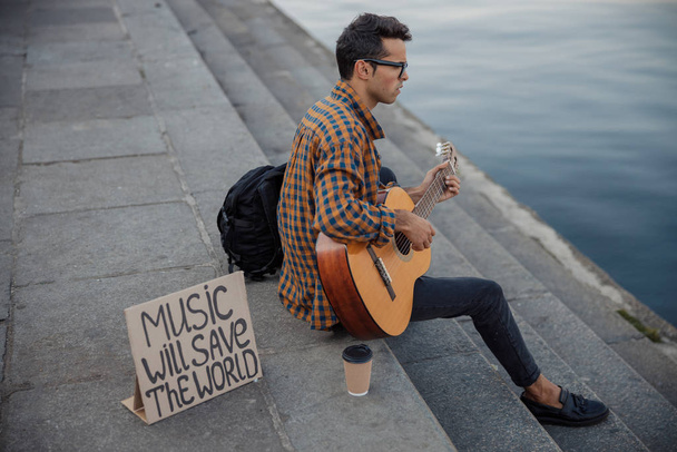 Young guitarist sitting near river on steps - Foto, Imagen