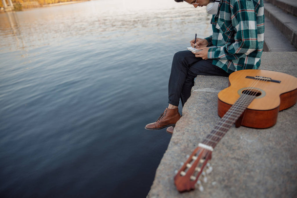 Young guitarist sitting with headphones and notebook outdoors - Foto, imagen