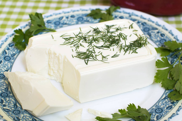 Φρέσκο ελληνικό τυρί φέτα. Υγιές συστατικό για σαλάτα μαγειρικής. Τυρί κατσικίσιο με μυρωδικά. Ένα κομμάτι φέτα σε ένα πιάτο με χόρτα άνηθου και μαϊντανού. - Φωτογραφία, εικόνα