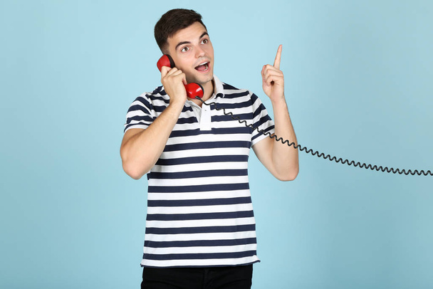 Young man with handset on blue background - 写真・画像