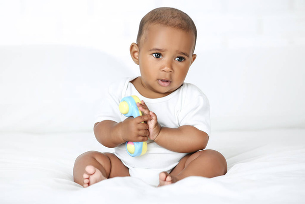 American baby girl sitting on white bed and holding toy - Foto, Bild