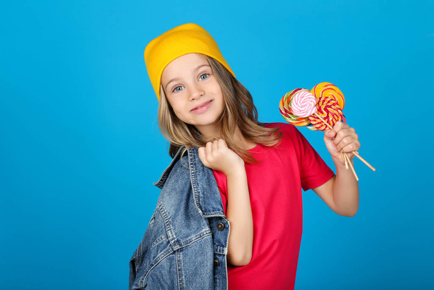Young girl in fashion clothing with colorful lollipops on blue background - Foto, Imagen