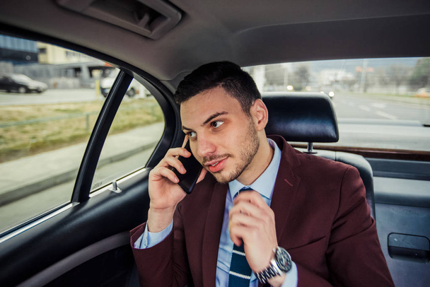 Modern businessman driving in a limo is having a phone conversation - Fotó, kép