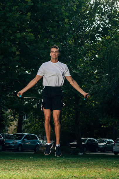 フィットネス、スポーツ、人、運動、ライフスタイルの概念-ジャンプロープを屋外でスキップする男 - 写真・画像