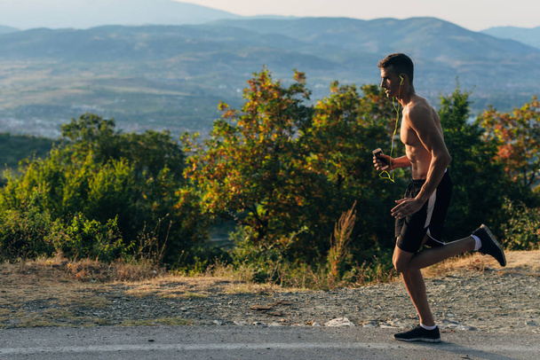 Porträt eines gesunden Sportlers mit Smartphone beim Joggen in der Natur bei blauem Himmel - Foto, Bild