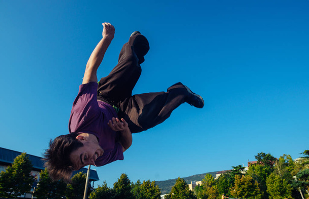 Jól megépített ember alatt egy oldalsó flip salto mozogni a levegőben a városi korcsolyapályán - Fotó, kép