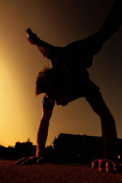 Acrobatic silhouette man exersicing parkour and gymnastic moves at a skatepark - 写真・画像
