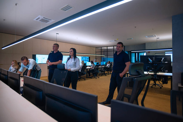 Biztonsági őrök állnak egy nagy CCTV monitor előtt a fő vezérlőteremben, miközben olvasnak és megbeszélik a terveket. - Fotó, kép